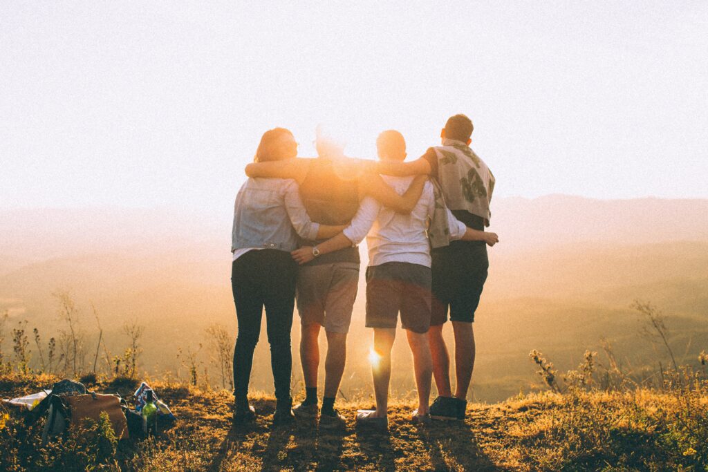 Group of friends with arms interlocked in front of a sunset on a cliff