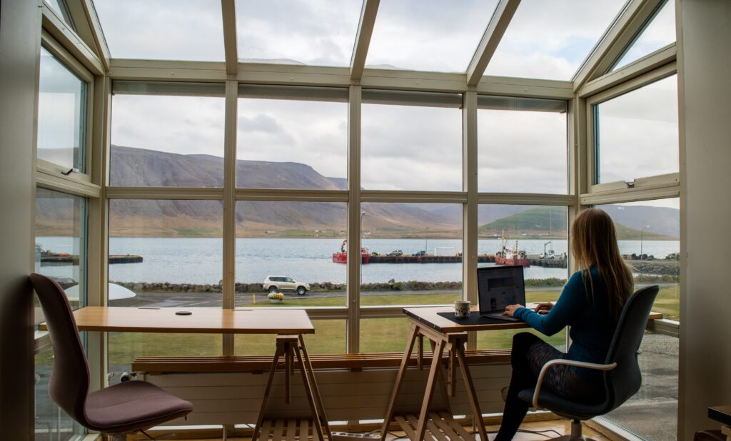 Woman with a laptop sitting at a table in front of a window with a lake landscape